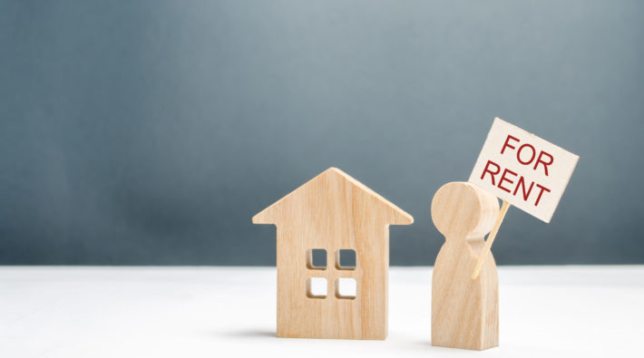 The figure of a man with a poster for rent stands near the house. Search for housing for rent or property rental. The concept of finding a roommate and making money on unused homes. Investments.